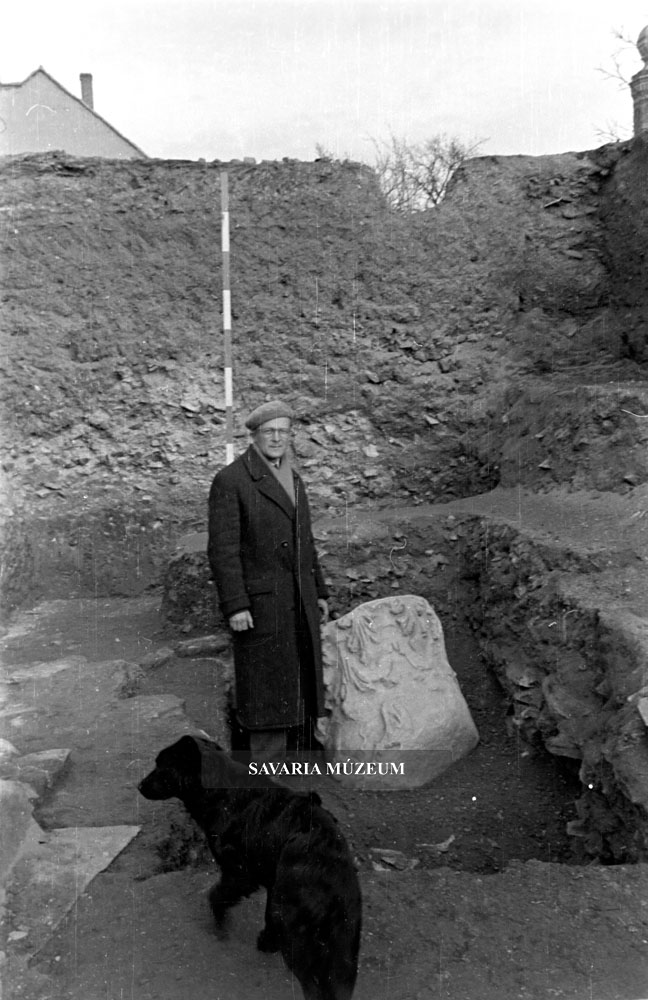 Szentléleky Tihamér ásatásvezető régész az Iseum udvarán Anubisz nevű kutyájával, egy törmelékgödörben fekvő márvány oszlopfő mellett.