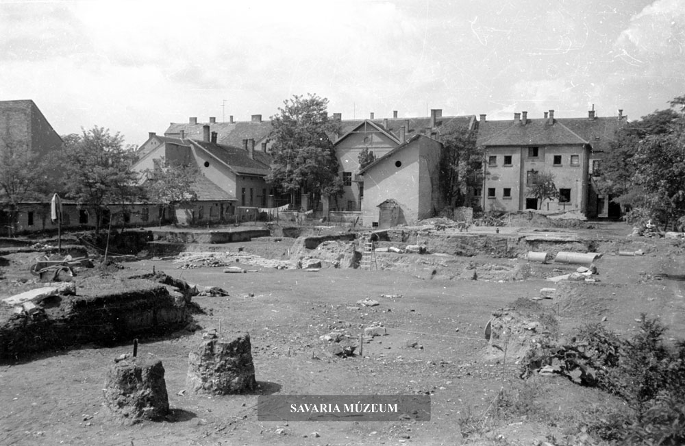 Az Iseum ásatása délről, a mai Képtár helyéről fotózva. Balra a honvédségi tekéző épülete, középen az Iseum maradványai gránitoszlopokkal és kőfaragványokkal. A fotó alapján érzékelhető az elvégzett földmunka óriási léptéke.