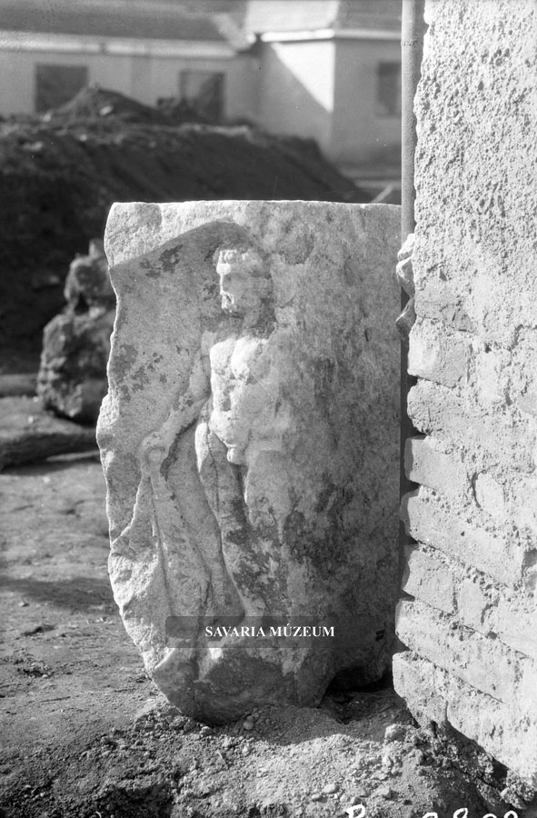 Hercules hősies alakja. Az 1955 novemberében előkerült Isis-Sothis márvány dombormű oldalsó díszítő eleme. A fülkében álló alak egykor a főhomlokzat északnyugati sarkát díszítette.